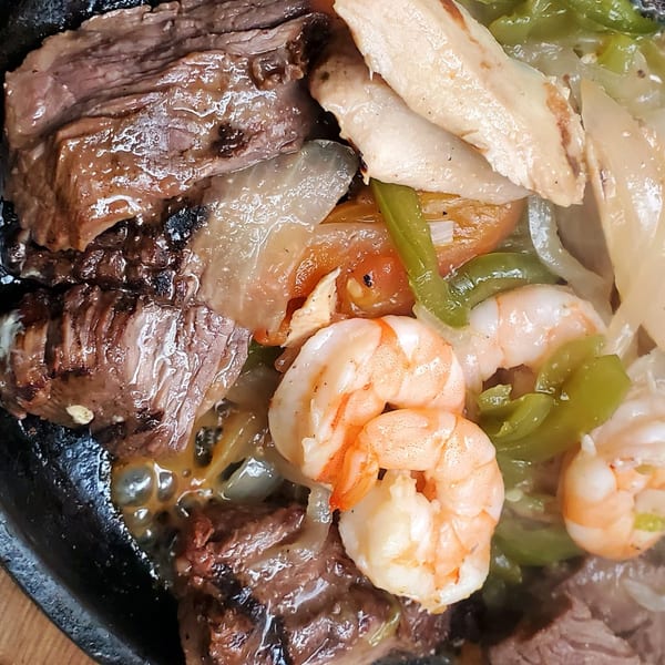 Sizzling fajitas with steak, chicken, shrimp, green peppers, and onions in a cast iron skillet.