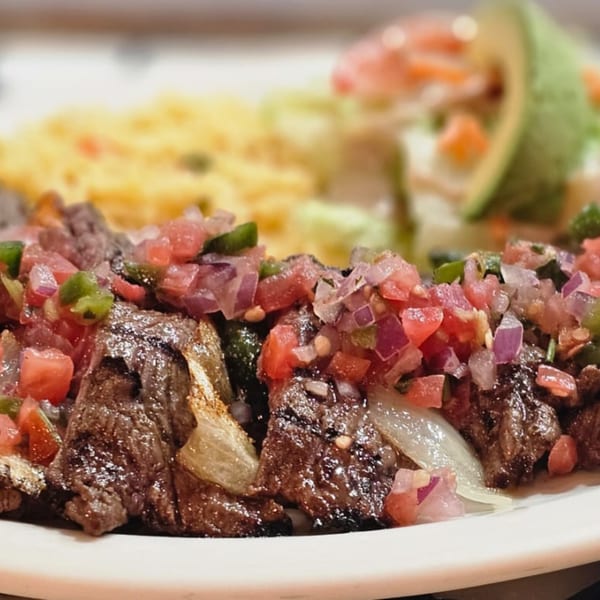 Grilled steak with pico de gallo, rice, and avocado slices on a white plate.