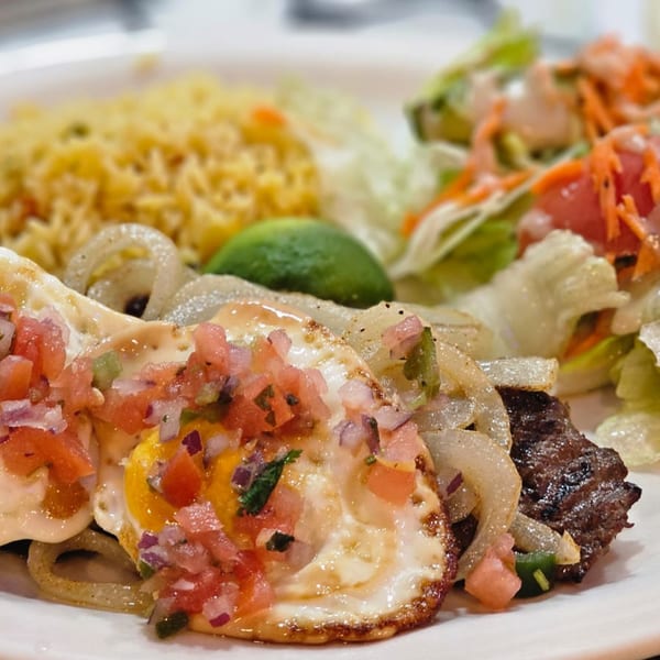 Two fried eggs topped with pico de gallo, alongside steak, rice, and a side salad.