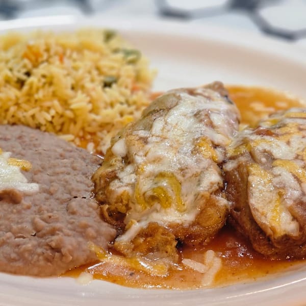 Two cheese-covered chiles rellenos with refried beans and yellow rice on a white plate.