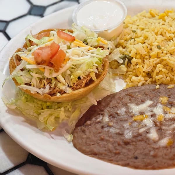 Crispy taco shell filled with meat, lettuce, tomato, and cheese, served with rice and refried beans.