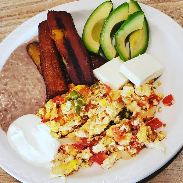 Mexican breakfast plate with scrambled eggs, refried beans, fried plantains, avocado slices, and cheese.