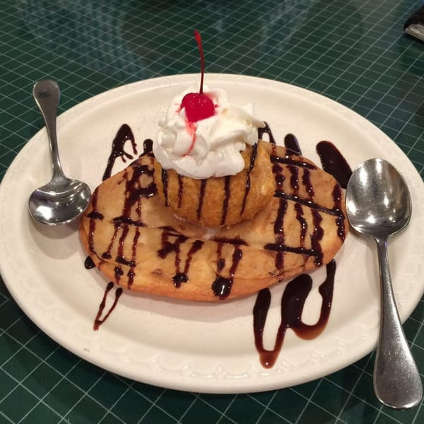 Fried ice cream with whipped cream and a cherry on top, drizzled with chocolate syrup.