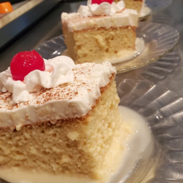 Three slices of tres leches cake with whipped cream, cinnamon, and a cherry on clear plates.